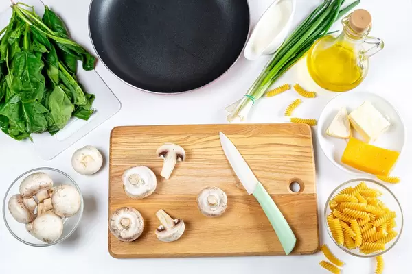 Konzeptbild zum Thema "Gesund kochen": Pastazubereitung mit Pilzen, Lauchzwiebeln, Spinat, Öl, Käse und Nudeln