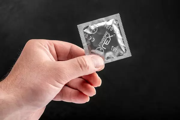 Konzeptbild zur individuellen Verhütung zeigt ein verpacktes Kondom in einer Männerhand, vor schwarzem Hintergrund