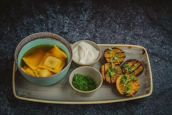 Kräftige Fleischbrühe mit Ravioli und gerösteten Brötchen auf Keramiktablett - Nahaufnahme in Draufsicht