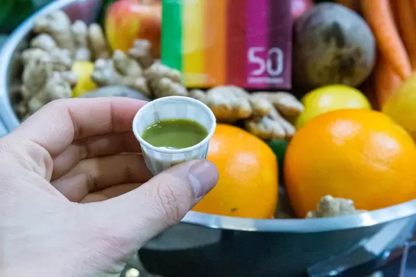 Kraftling ingwershot in der Hand gehalten vor Frucht und Gemüsekorb