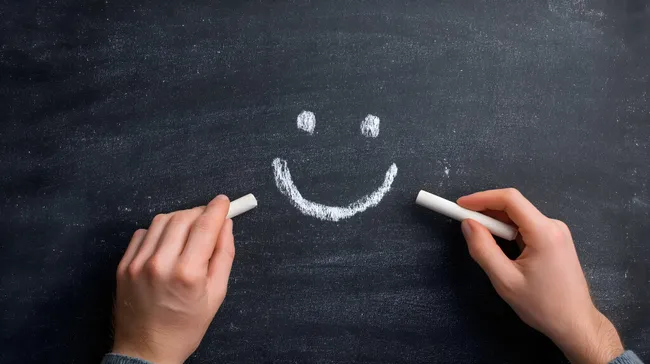 Kreide-Smiley auf schwarzer Schultafel mit Händen