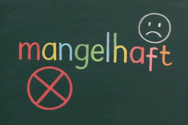 Kreideschrift an Tafel: 'Mangelhaft' mit traurigem Smiley