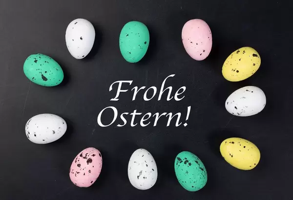 Kreis aus bunten Ostereiern um weißen Text FROHE OSTERN auf schwarzem Hintergrund