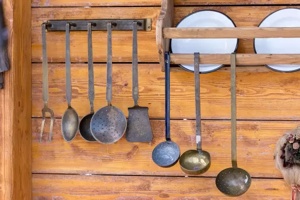 Küchenutensilien aus Metall hängen an einer Holzwand