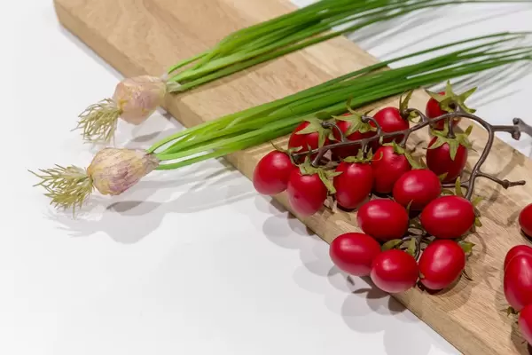 Künstliche ganze Frühlingszwiebeln mit Stängeln und Tomaten an Strauch auf Holzbrett