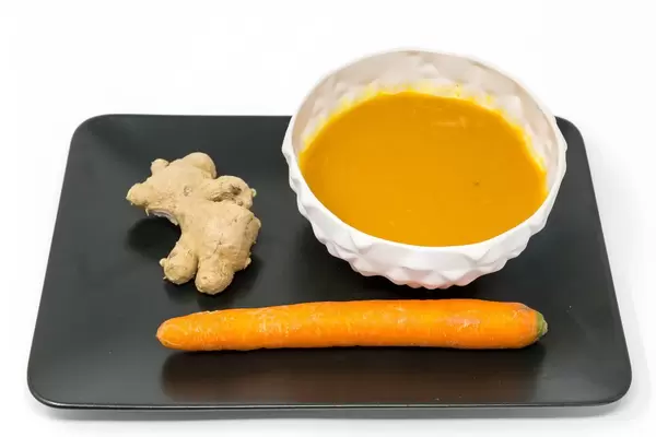 Kürbis-Kokosnuss-Cremesuppe mit Inger auf einem schwarzen Teller mit einer Ingwerwurzel und einer Möhre