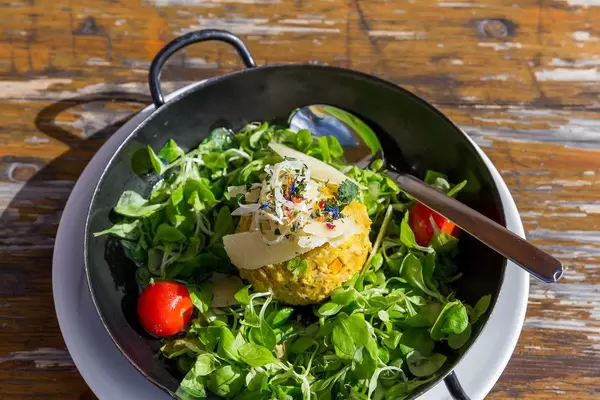 Kürbisknödel mit Feldsalat, Parmesan-Käse und Cherry-Tomaten. Pfanne auf hölzernem Tisch