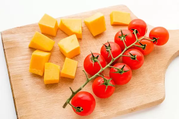 Kürbisstücke und eine Staude Kirschtomaten auf einem Holzbrettchen
