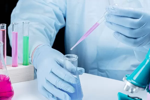 Laboratory assistant in gloves with a flask and pipette working at the table (Flip 2020)