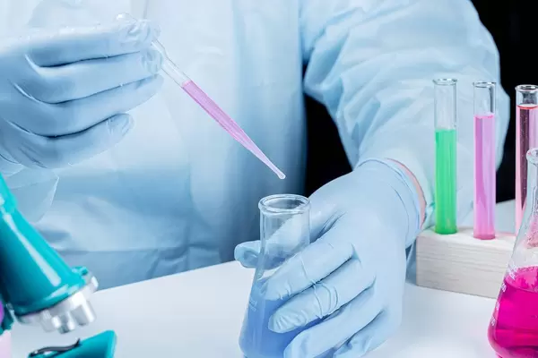 Laboratory assistant in gloves with a flask and pipette working at the table