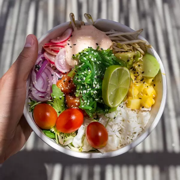 Lachs-Poke-Bowl mit Reis, Limette, Kirschtomaten, Radieschen, Sprossen, Avocado, Kräutern. Draufsicht