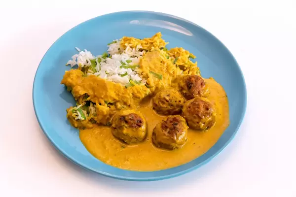 Lachsbällchen mit Zuckerschottenreis und Soße auf blauem Teller vor weißem Hintergrund