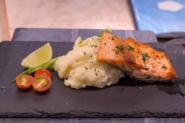 Lachsfilet mit Kartoffelstock, Tomaten und Limette auf Steinplatte serviert