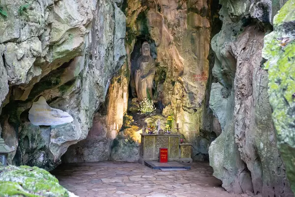 Lady Buddha Statue carved in a Stone Wall inside a Cave with Offerings and Donation Box in front at Marble Mountains, Vietnam