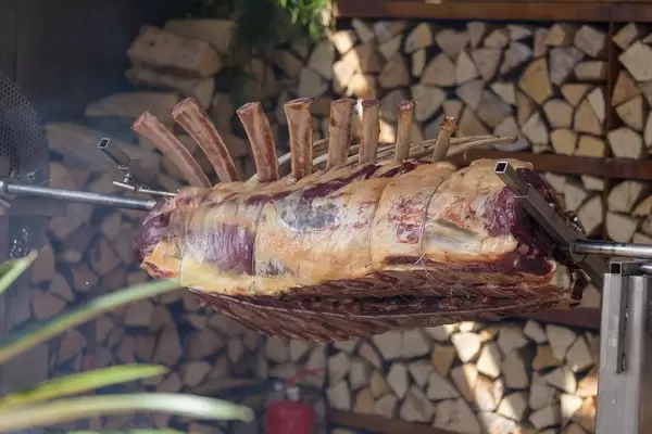 Lammrack, auch Lammrücken genannt, auf elektrischem Drehspieß vor Stapel von Holzscheiten