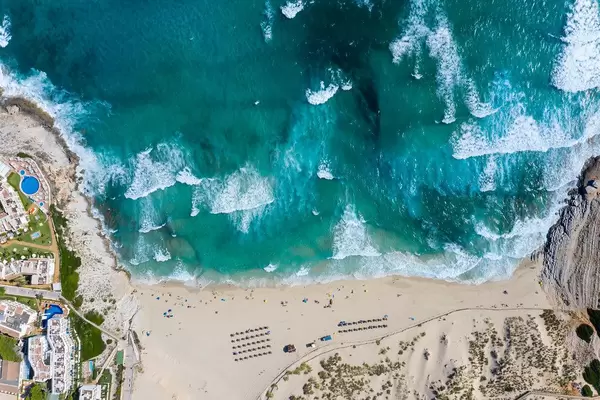 Langer Sandstrand mit Dünen und Wellen. Drohnenaufnahme von Cala Mesquida auf Mallorca