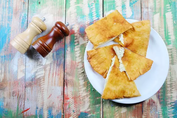 Langos aus Ungarn mit Käse, Salz und Pfeffer auf einem bunten Holztisch im Vintage-Stil