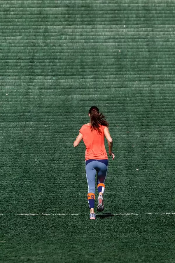 Läuferin in Sportklamotten läuft beim Ausdauertraining eine grüne Skisprungschanze der Salpausselkä-Schanzenanlage hoch