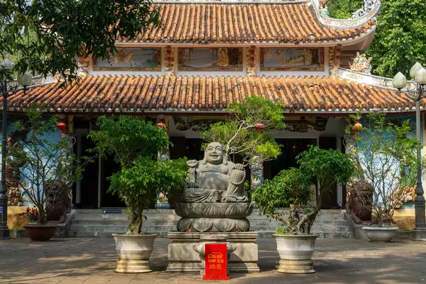 Laughing Buddha Statue with Donation Boxand Trees in Plant Pots in front of Tam Thai Pagoda at Marble Mountains in Da Nang, Vietnam