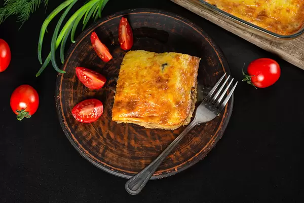 Layered casserole with meat, cheese and mushrooms on a plate with fresh tomato slices