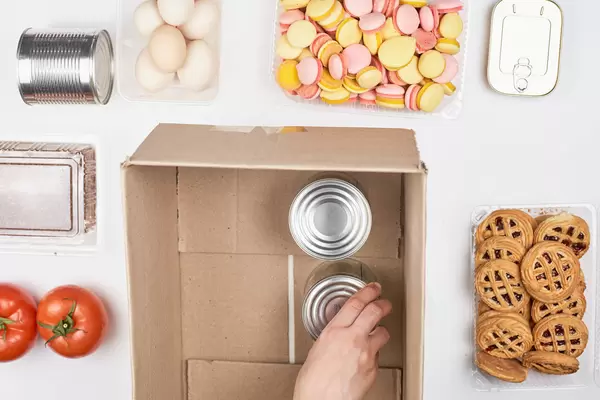 Lebensmittel wie Tomaten, Eier und Süßigkeiten spenden, Blechdosen in einen Karton stellen