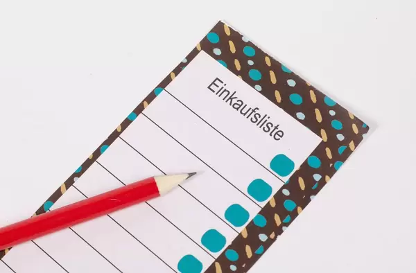 Leere Einkaufsliste auf buntem Notizblock mit Bleistift auf weißem Tisch