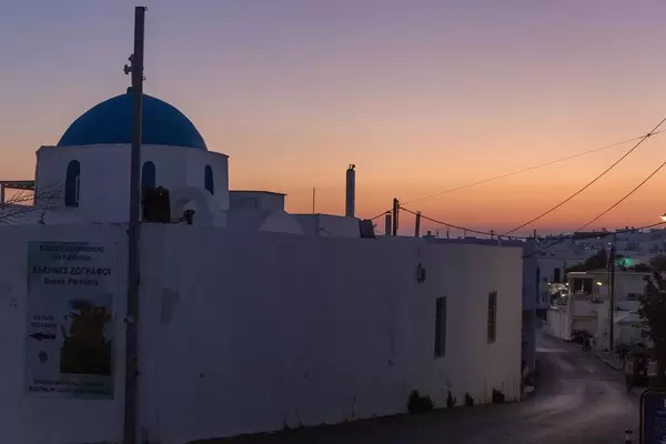 Leere Straße bei Nacht, mit orangem Himmel und weißer Kirche auf der griechischen Insel Paros