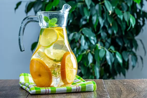 Lemonade in jar with ice and mint on a wooden table, behind a green tree (Flip 2019)