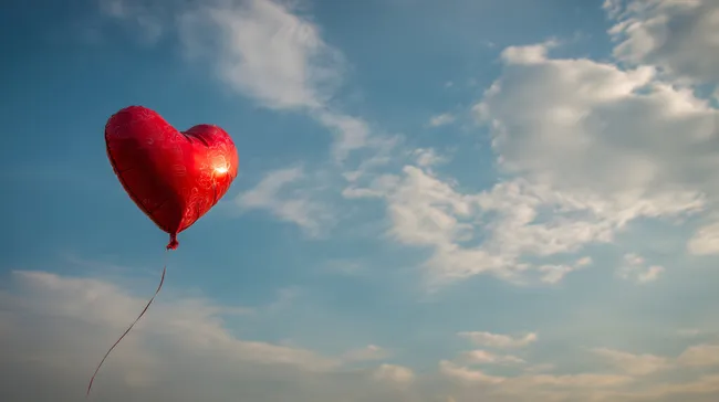 Leuchtend rotes Herz-Luftballon im Sommerhimmel