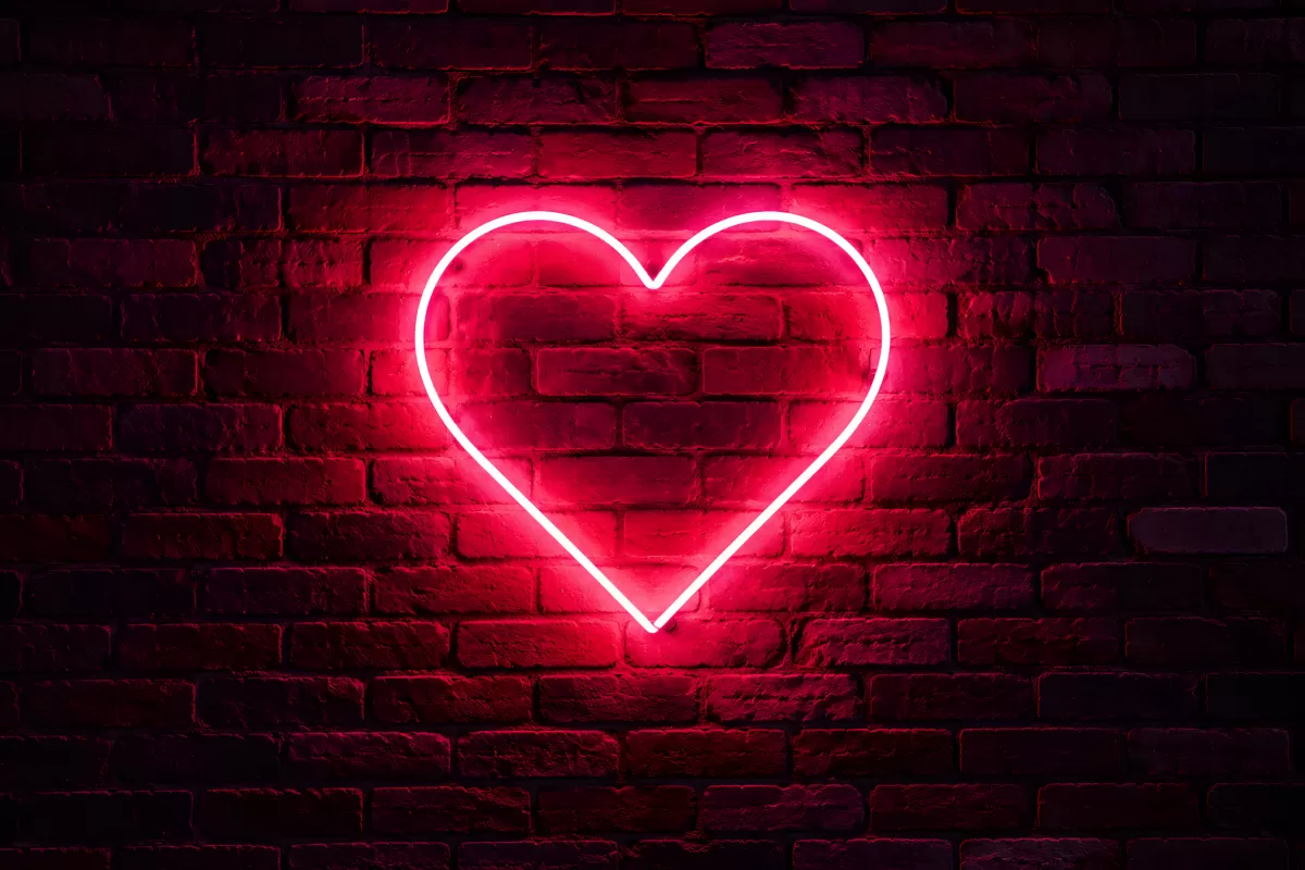 Leuchtendes Neon-Herz an roter Backsteinwand