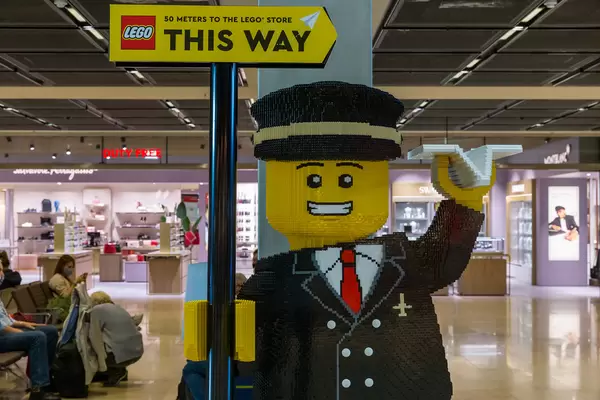 Life-size LEGO figure of airplane pilot holding a sign indicating directions to the BER airport LEGO Store