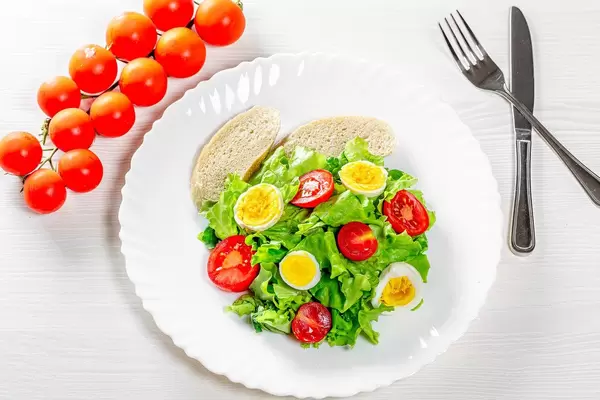 Light salad with herbs, tomatoes, boiled eggs and breadcrumbs on a white table