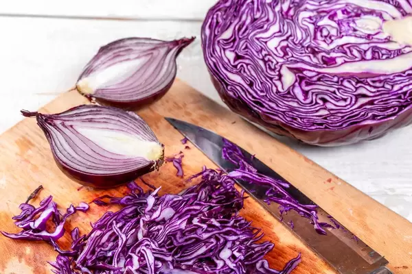 Lila Rotkohl und rote Zwiebeln, halbiert, neben einem schwarzen Küchenmesser