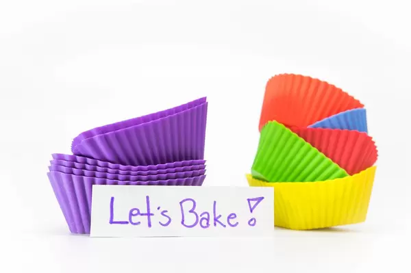 Lila und bunte Cupcake-Förmchen zum Backen mit Notizzettel und dem Text "Let's bake!"