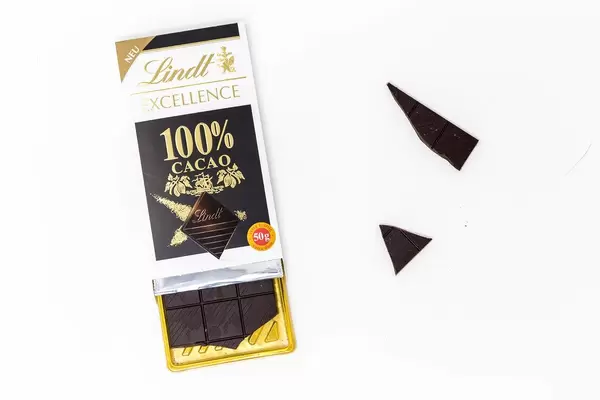 Lindt Excellence 100% Kakao Schokoladentafel, schon angebrochen mit losen Schokoladenstücke vor weißem Hintergrund
