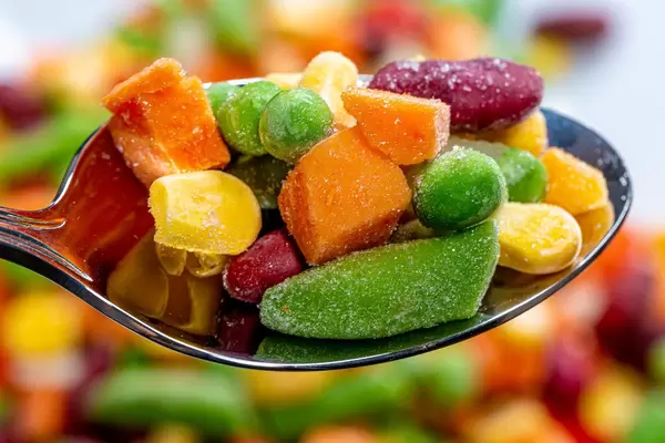 Löffel mit Erbsen, Mais, Bohnen und Karotten in der Nahaufnahme