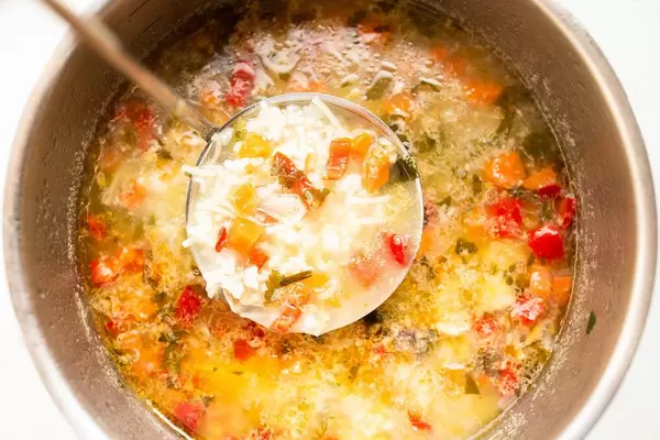 Löffel schöpft Reissuppe mit Hühnchen und Gemüse aus Topf vor weißem Hintergrund