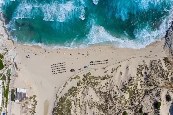 Long stretch of sandy beach with dunes and waves. Overhead drone shot of Cala Mesquida in Majorca