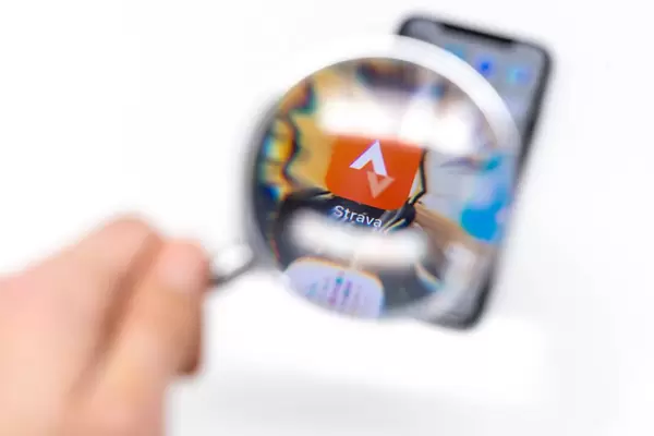 Looking through magnifying glass on Strava app on black cellphone in front of white background