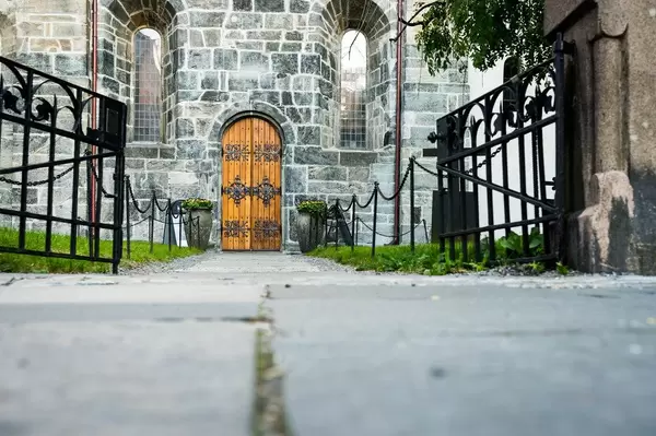 Low view of wooden church door with an open forged iron gate in foreground (Flip 2019)