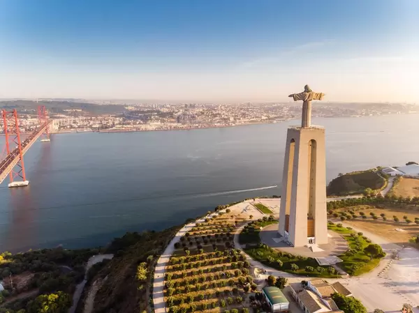 Luftaufnahme der Cristo Rei Statue von hinten mit Ponte 25 de abril Brücke in Almada Lissabon
