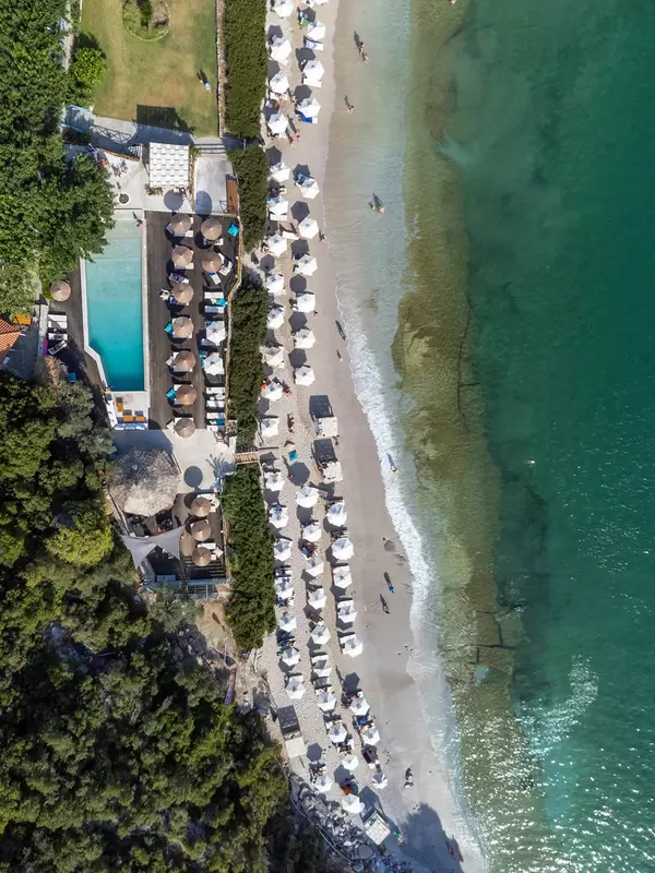Luftaufnahme des Limnonari-Strandes mit weißen sechseckigen und Stroh-Sonnenschirmen und Schwimmbad