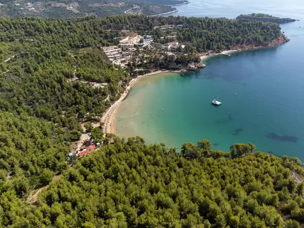 Luftaufnahme des Strandes und der Bucht von Chrisi Milia mit einem Katamaran im türkisfarbenen Meer