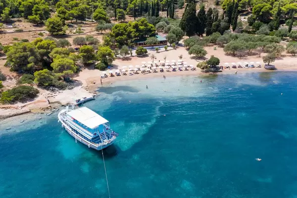 Luftaufnahme einer blauen Inselfähre im blauen Meer, am Sandstrand Zogeria von Spetses, Griechenland