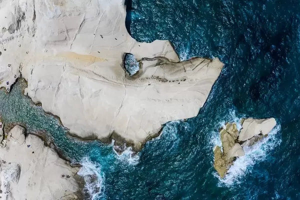 Luftaufnahme von der Küste auf Milos mit schmaler Bucht und großem Loch in der weißen Felswand
