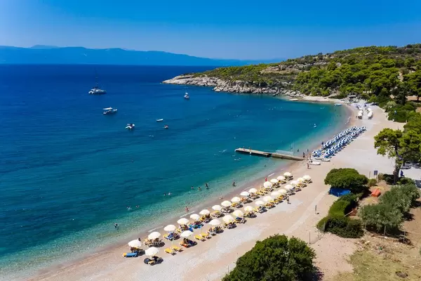 Luftaufnahme von gelben und blauen Liegestühlen in einer Reihe, unter Sonnenschirmen, an einem Strand in Agii Anargiri, am Myrtoischen Meer