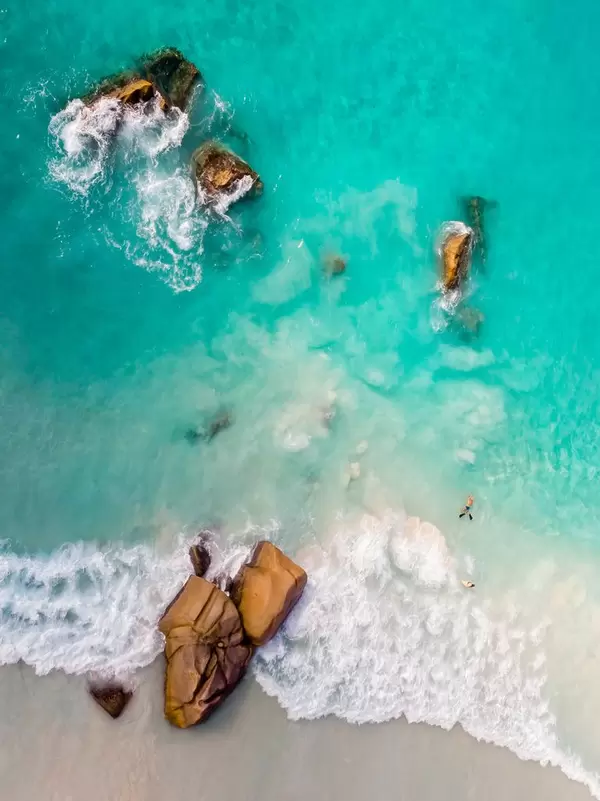 Luftaufnahme von Granitfelsen im grünen Meer und seichten Wellen am Strand von Anse Lazio auf Praslin, Seychellen