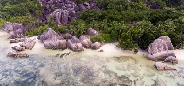Luftaufnahme von mehrfarbigen Granitfelsen zwischen Tropenbäumen und Palmen am Anse Union-Strand auf La Digue, Seychellen
