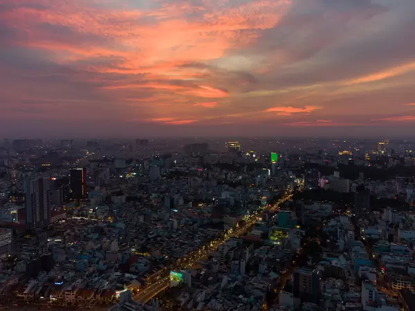 Luftaufnahme von vielen Gebäuden und beleuchteten Straßen bei Sonnenuntergang mit farbenfrohem Himmel in Ho Chi Minh Stadt, Vietnam