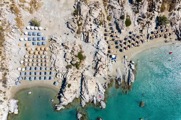 Luftaufnahme zeigt den Felsenstrand Kolimbithres auf Paros, mit Sonnenschirmen am weißen Sandstrand am grünen Mittelmeer